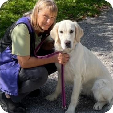 Nancy Hatch from Partner Dogs Canada kneeling beside a trained Golden Retriever during a service dog training session outdoors.